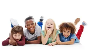 Diversity, children and happy friends or fun on the floor together or against a white background and hug. Smile, kids and playful or laughing and isolated in studio or excited buddies and embrace.